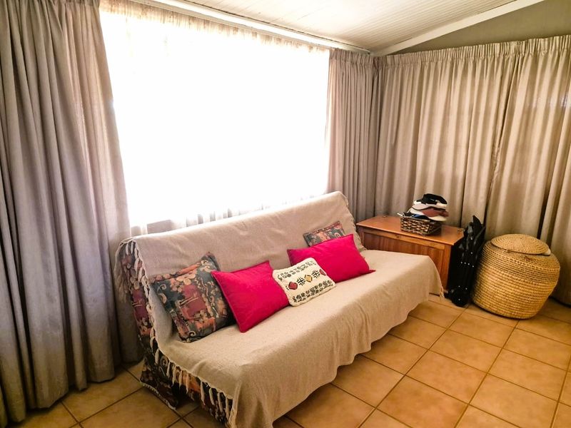 A living area featuring tiled flooring and a large window with full-length curtains, offering a bright and functional space.
