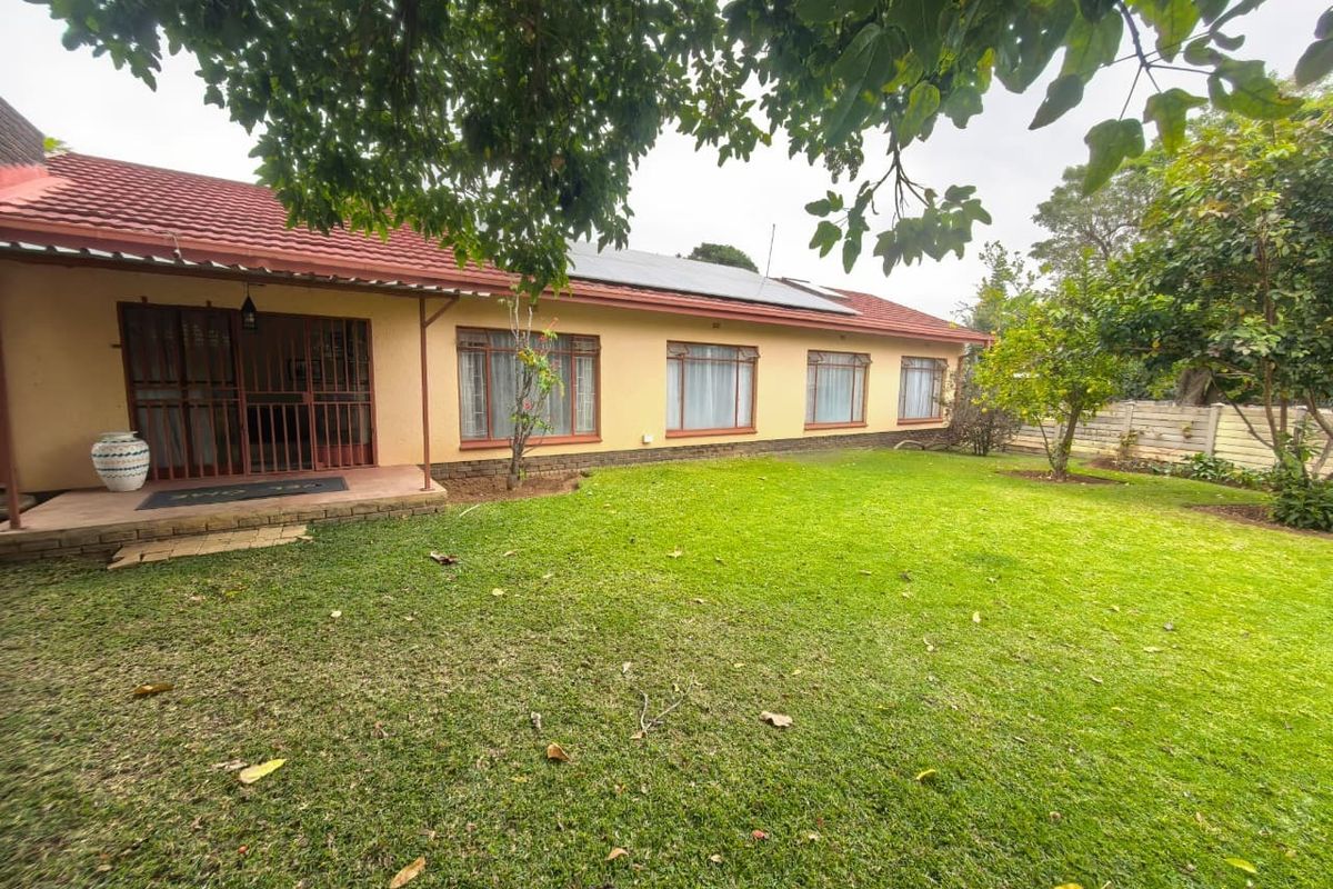 Rear view of the house featuring a tiled roof with solar panels, a spacious lawn, and a covered patio area with security gates.