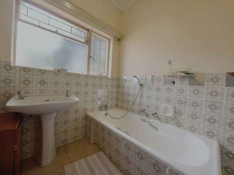 A functional bathroom featuring a pedestal basin, a built-in bathtub with a handheld shower mixer, and classic patterned wall tiling.