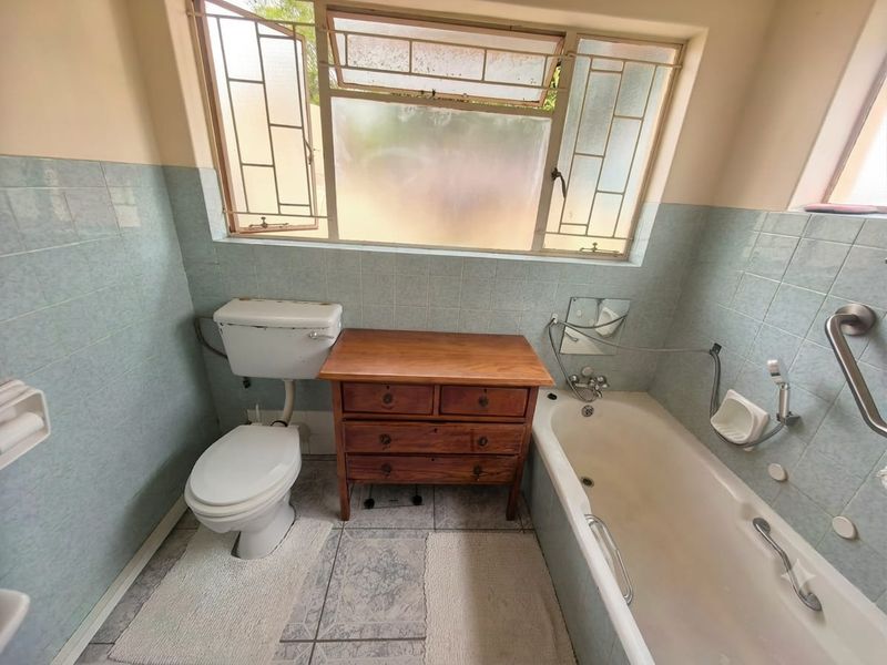 A dated bathroom featuring a standard bathtub, toilet, and light blue wall tiling, requiring modernization of fixtures and finishes.