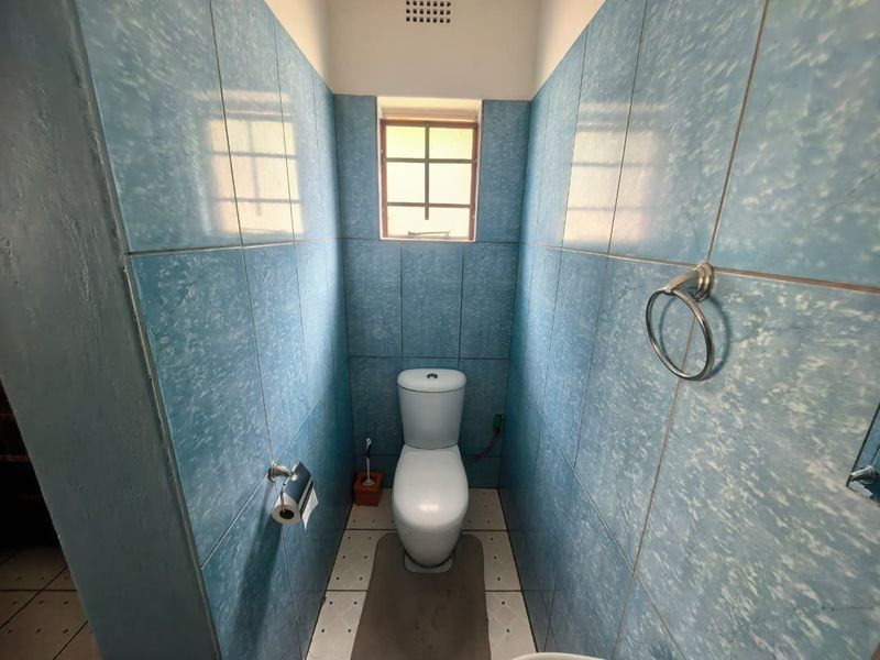 A compact, dated bathroom featuring blue wall tiles, a standard toilet, and a small window for natural light.