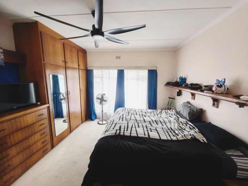 A bedroom featuring a large built-in wooden wardrobe, a ceiling fan, and a wall-mounted wooden shelf, providing functional storage and comfort.