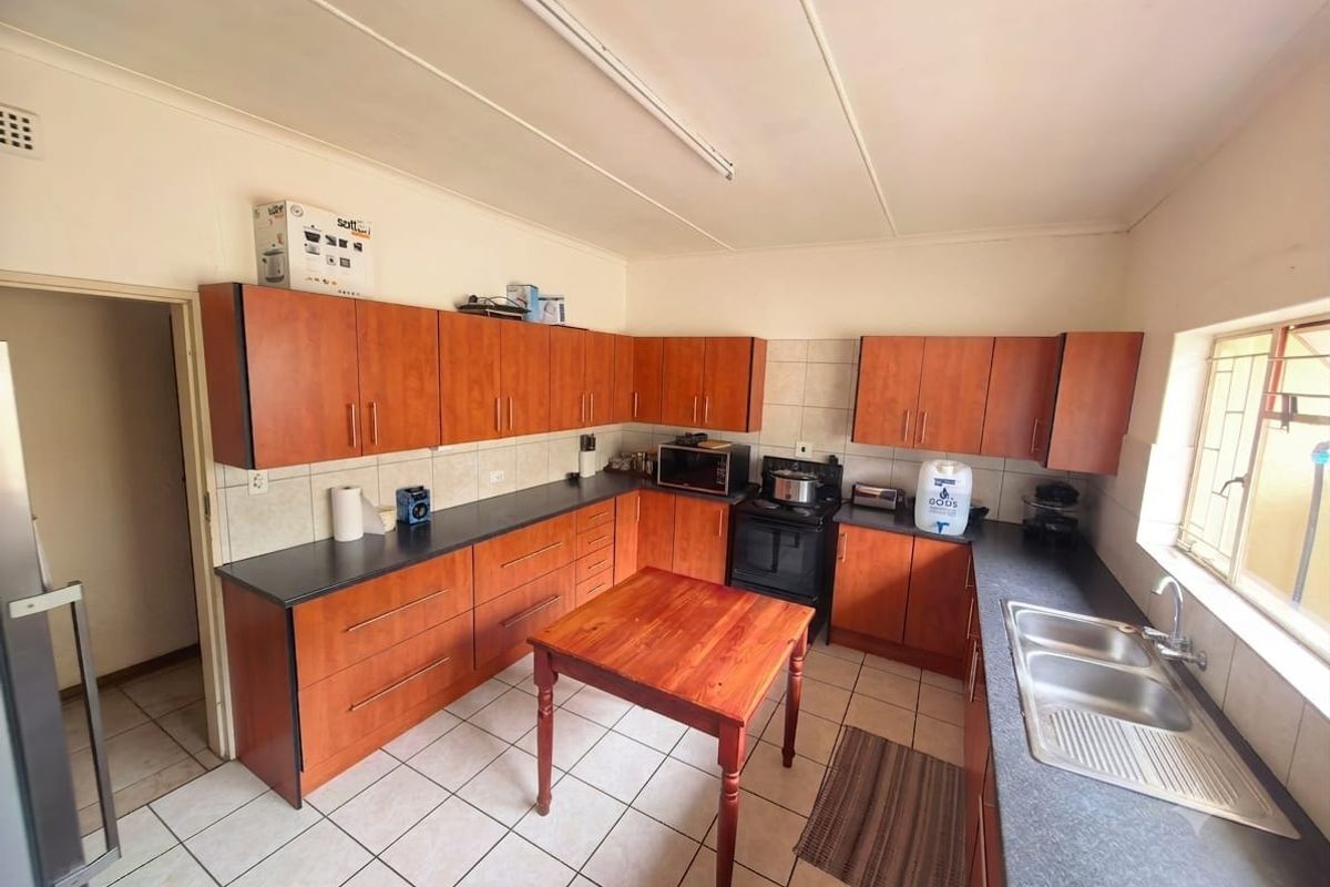 Functional kitchen featuring wood-look laminate cabinetry, dark countertops, a double stainless steel sink, and ceramic floor tiling.