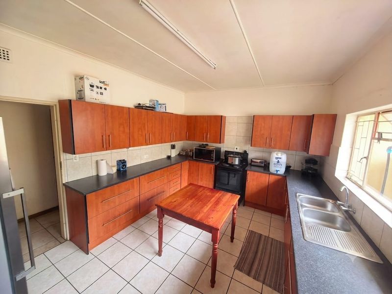 Functional kitchen featuring wood-look laminate cabinetry, dark countertops, a double stainless steel sink, and ceramic floor tiling.