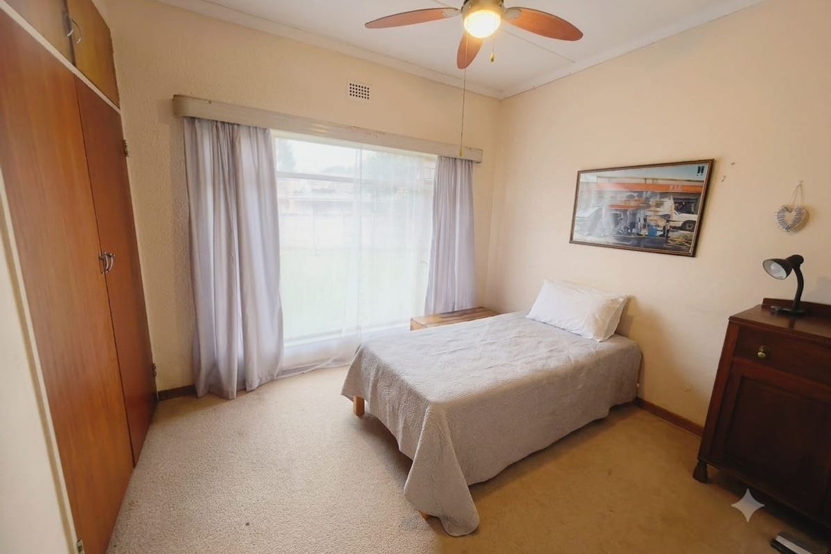 A functional bedroom featuring built-in wooden cupboards, a ceiling fan, and large windows allowing natural light.
