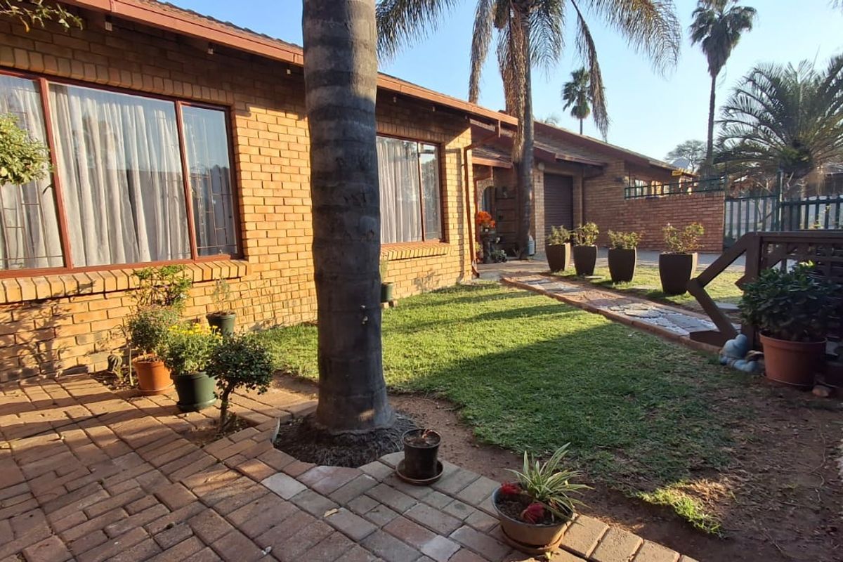 A rear exterior view of a face brick townhouse featuring a paved patio area, a small lawn, and a timber deck section.