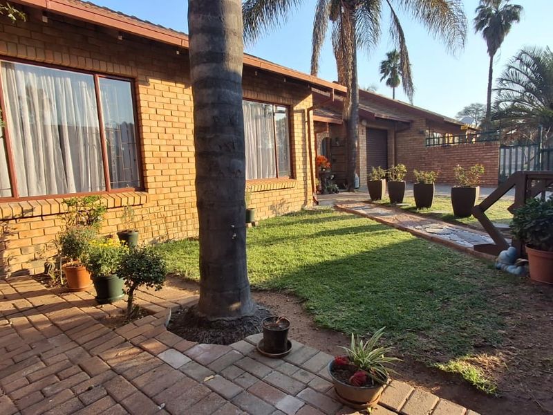 A rear exterior view of a face brick townhouse featuring a paved patio area, a small lawn, and a timber deck section.