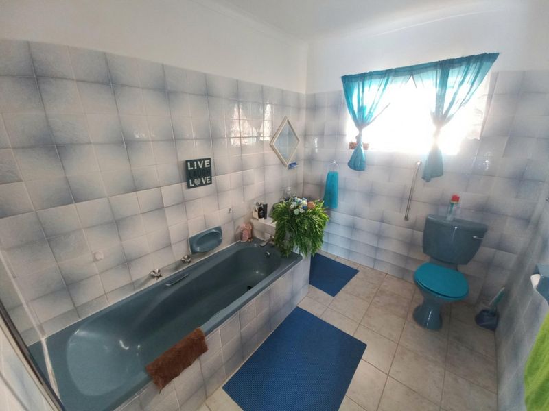 A functional bathroom featuring a built-in bathtub, toilet, and tiled finishes. The space is dated and would benefit from modern updates.