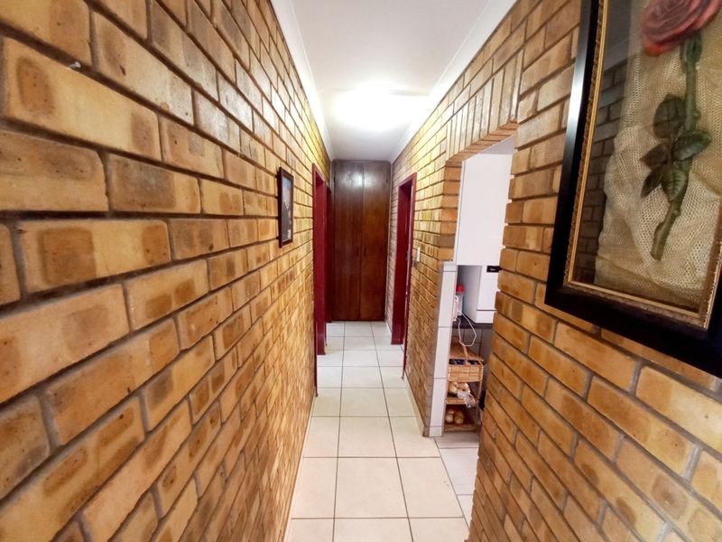 A hallway featuring exposed brick walls, tiled flooring, and a built-in storage cupboard, providing access to adjacent rooms.