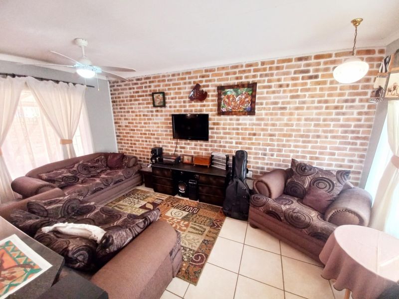 A comfortable living room featuring a prominent exposed brick feature wall, tiled flooring, and a ceiling fan, providing a warm and inviting atmosphere.