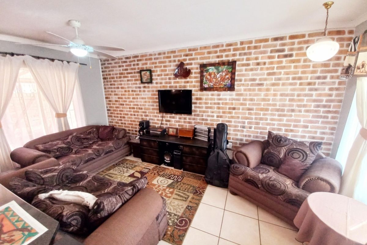 A comfortable living room featuring a prominent exposed brick feature wall, tiled flooring, and a ceiling fan, providing a warm and inviting atmosphere.