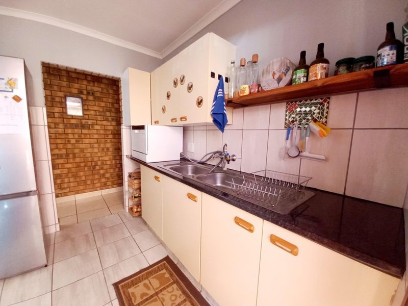 A functional kitchen featuring built-in cabinetry, a double bowl sink, tiled backsplash, and a distinctive exposed brick wall section.