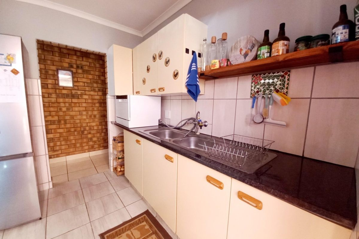 A functional kitchen featuring built-in cabinetry, a double bowl sink, tiled backsplash, and a distinctive exposed brick wall section.