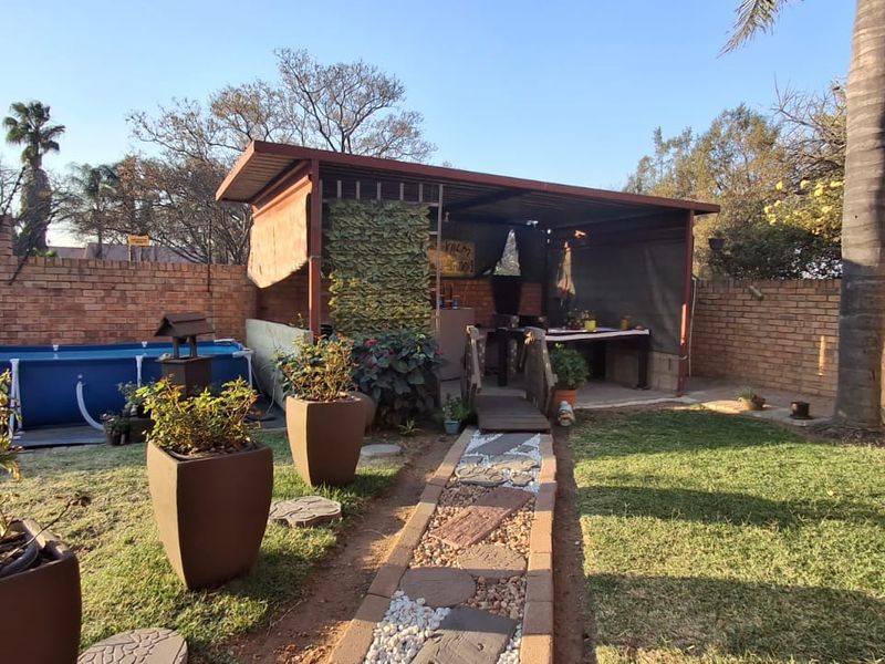 Outdoor entertainment area featuring a covered patio, paved garden path, and brick boundary walls in a private backyard setting.
