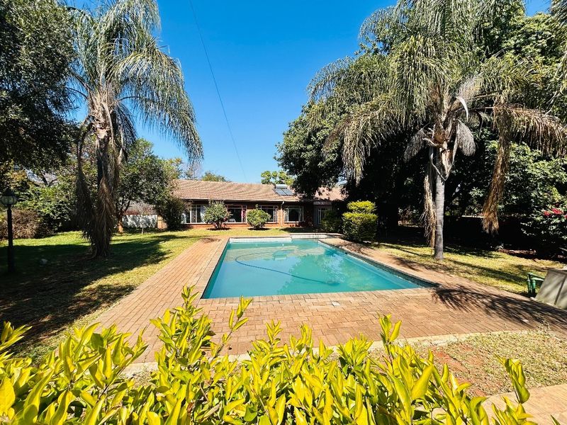A spacious backyard featuring a swimming pool with brick paving, surrounded by mature trees and a well-maintained garden.