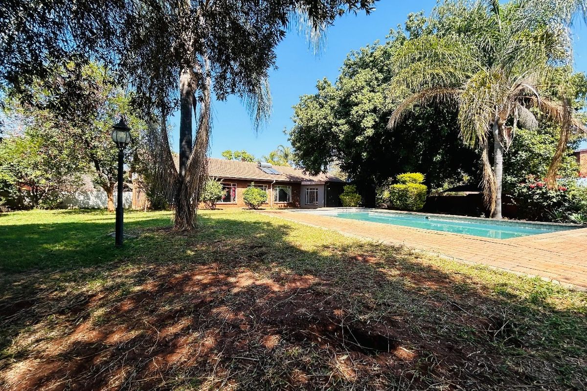 Rear view of the property featuring a swimming pool, brick paved surround, and established garden with mature trees.