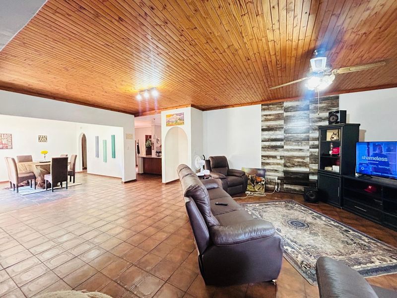 Spacious open-plan living and dining area featuring a warm timber-clad ceiling, ceramic tiled flooring, and a decorative feature wall.