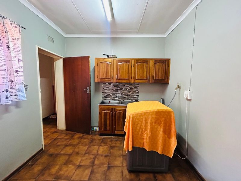 A functional laundry room featuring built-in wooden cabinetry, a double basin sink with tiled splashback, and durable ceramic floor tiles.