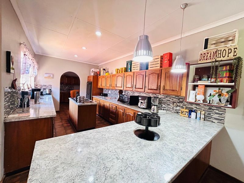 Spacious kitchen featuring wooden cabinetry, laminate countertops, a central island, and a mosaic tile backsplash, with an archway leading to an adjacent area.
