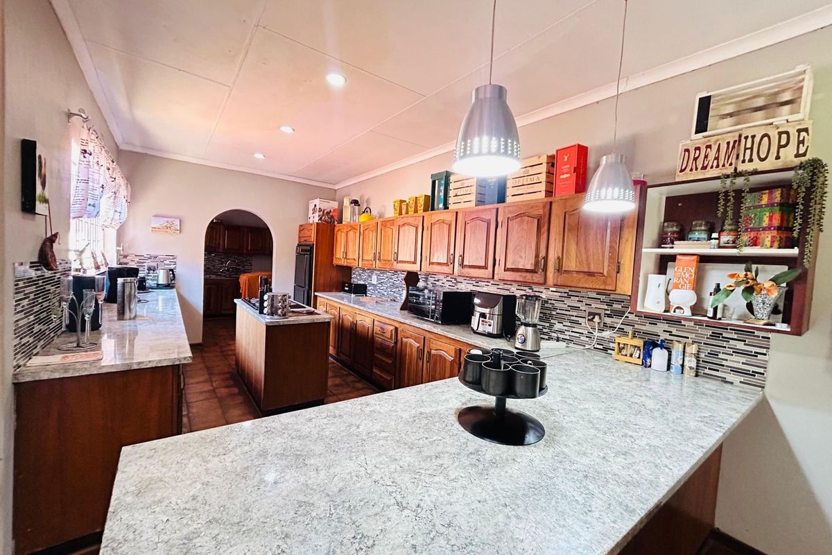 Spacious kitchen featuring wooden cabinetry, laminate countertops, a central island, and a mosaic tile backsplash, with an archway leading to an adjacent area.