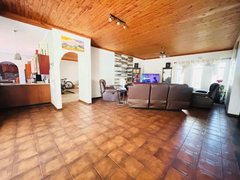Spacious open-plan living area featuring a timber-clad ceiling, ceramic floor tiles, and a stone-accented feature wall, connecting seamlessly to the adjacent kitchen space.