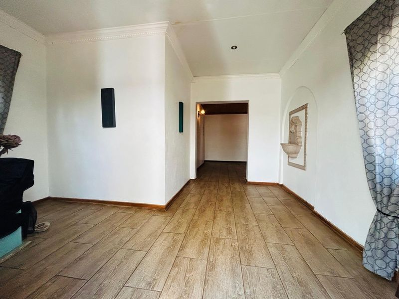 A spacious, neutral hallway featuring wood-look tiled flooring, a decorative wall niche, and coved ceiling detailing, leading into an adjacent living area.