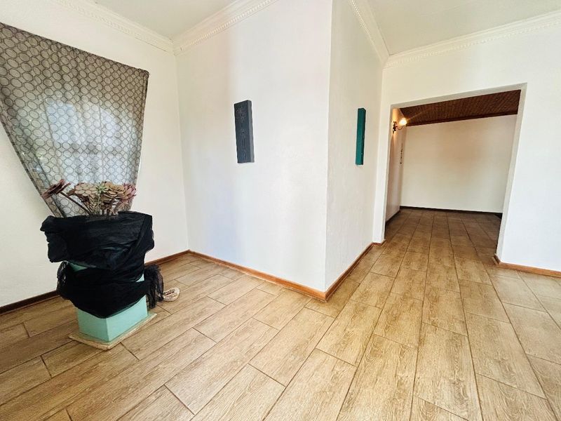 A bright, empty hallway featuring wood-look tiled flooring, crown molding, and an open archway leading to an adjacent room.