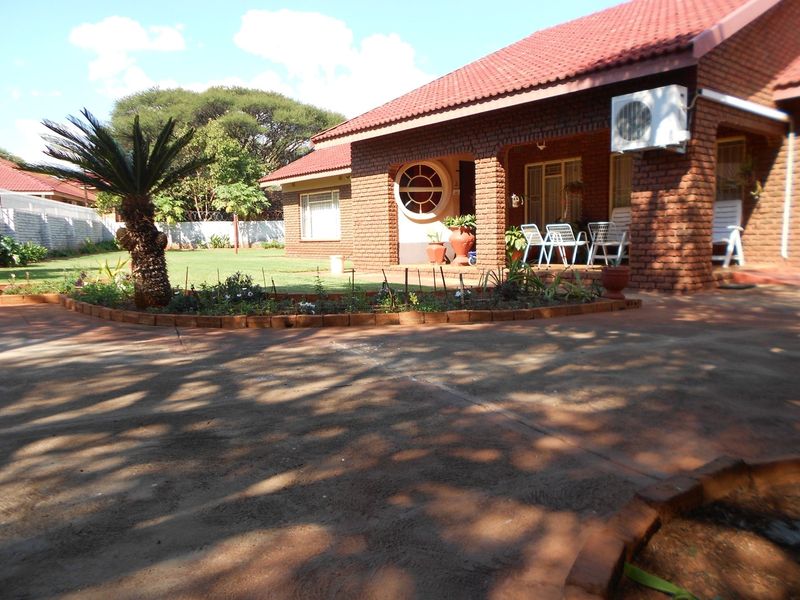 A front view of a face brick house featuring a tiled roof, covered patio, air conditioning unit, and a well-maintained garden with a paved driveway.