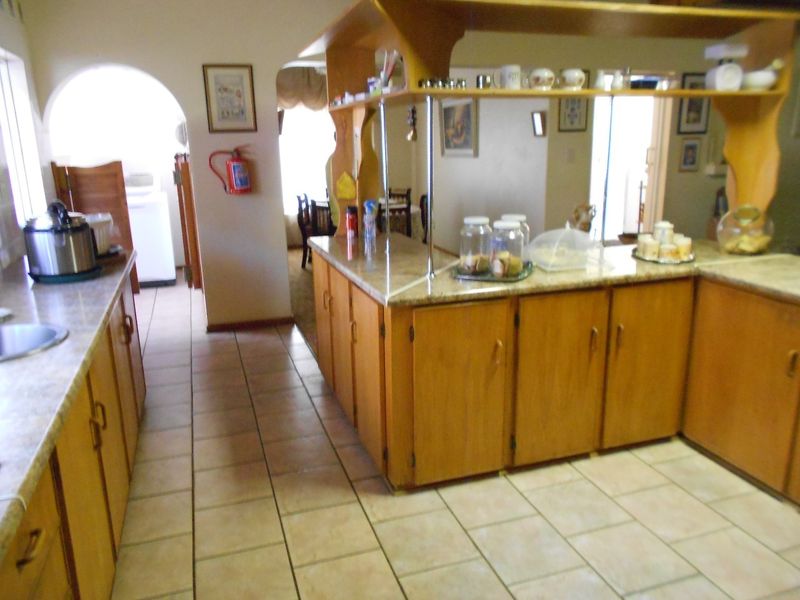 A functional kitchen featuring wooden cabinetry, stone-look laminate countertops, and ceramic floor tiles, with an open-plan layout connecting to adjacent living areas.