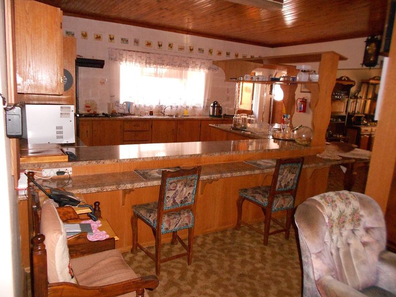 Open plan kitchen featuring wooden cabinetry, laminate countertops, and a breakfast bar, with a distinctive wooden ceiling and dated finishes throughout.