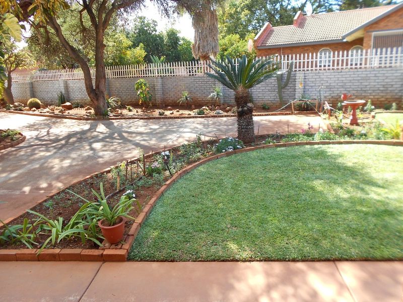 A well-maintained garden featuring a manicured lawn, brick-edged garden beds, and a paved driveway enclosed by a secure brick boundary wall.