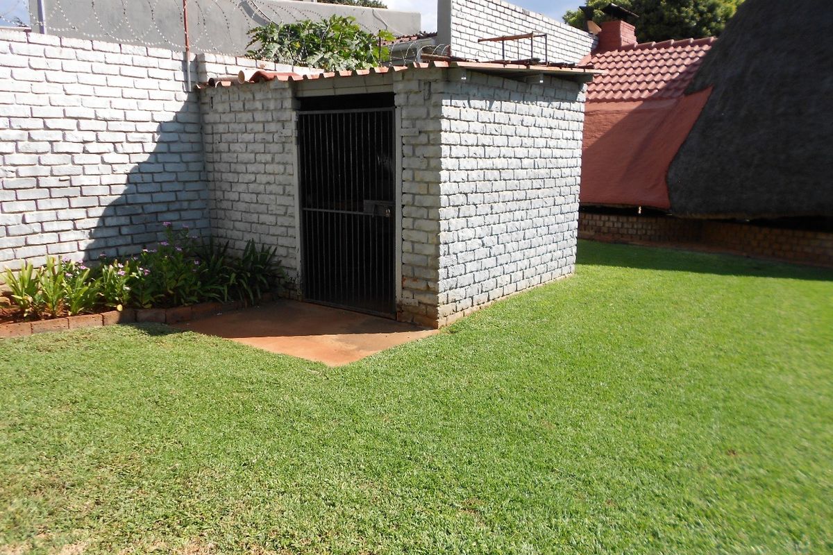 A rear garden area featuring a small brick utility shed with a security gate, enclosed by a brick boundary wall with razor wire.