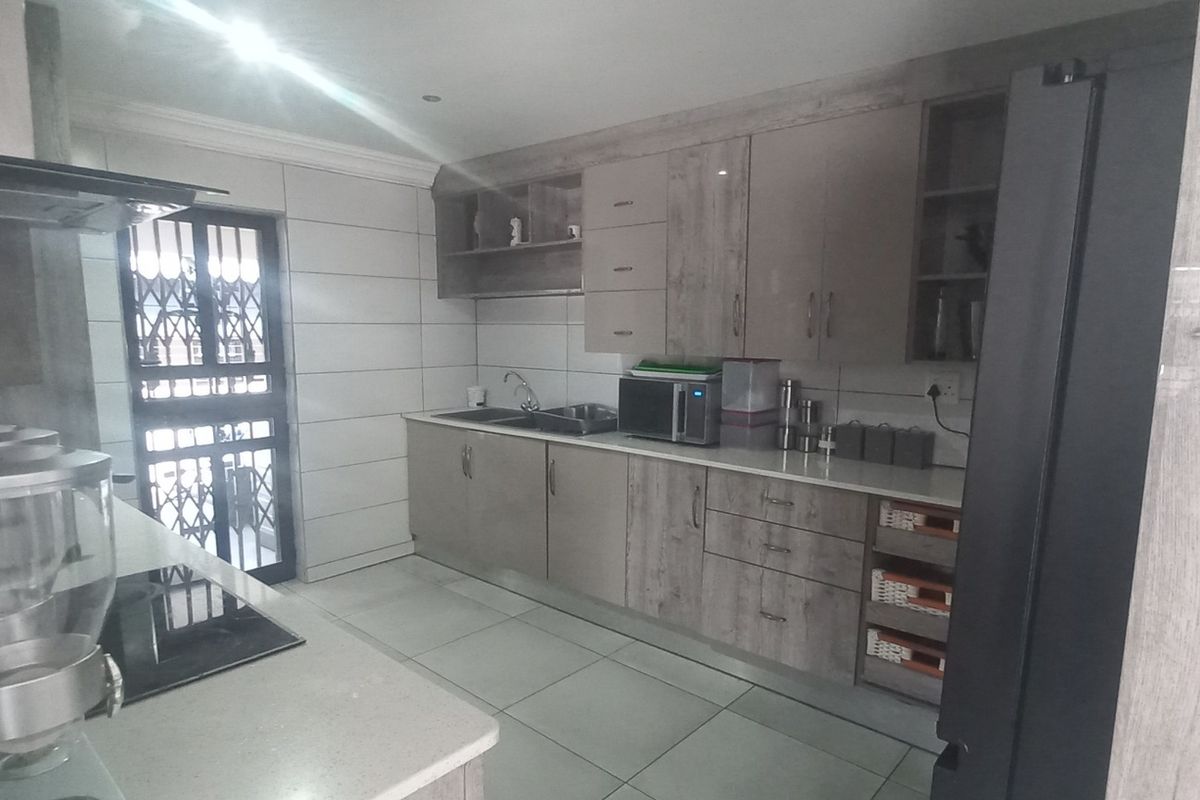 Modern kitchen featuring wood-grain cabinetry, stone countertops, integrated hob with extractor fan, and large format floor tiles.