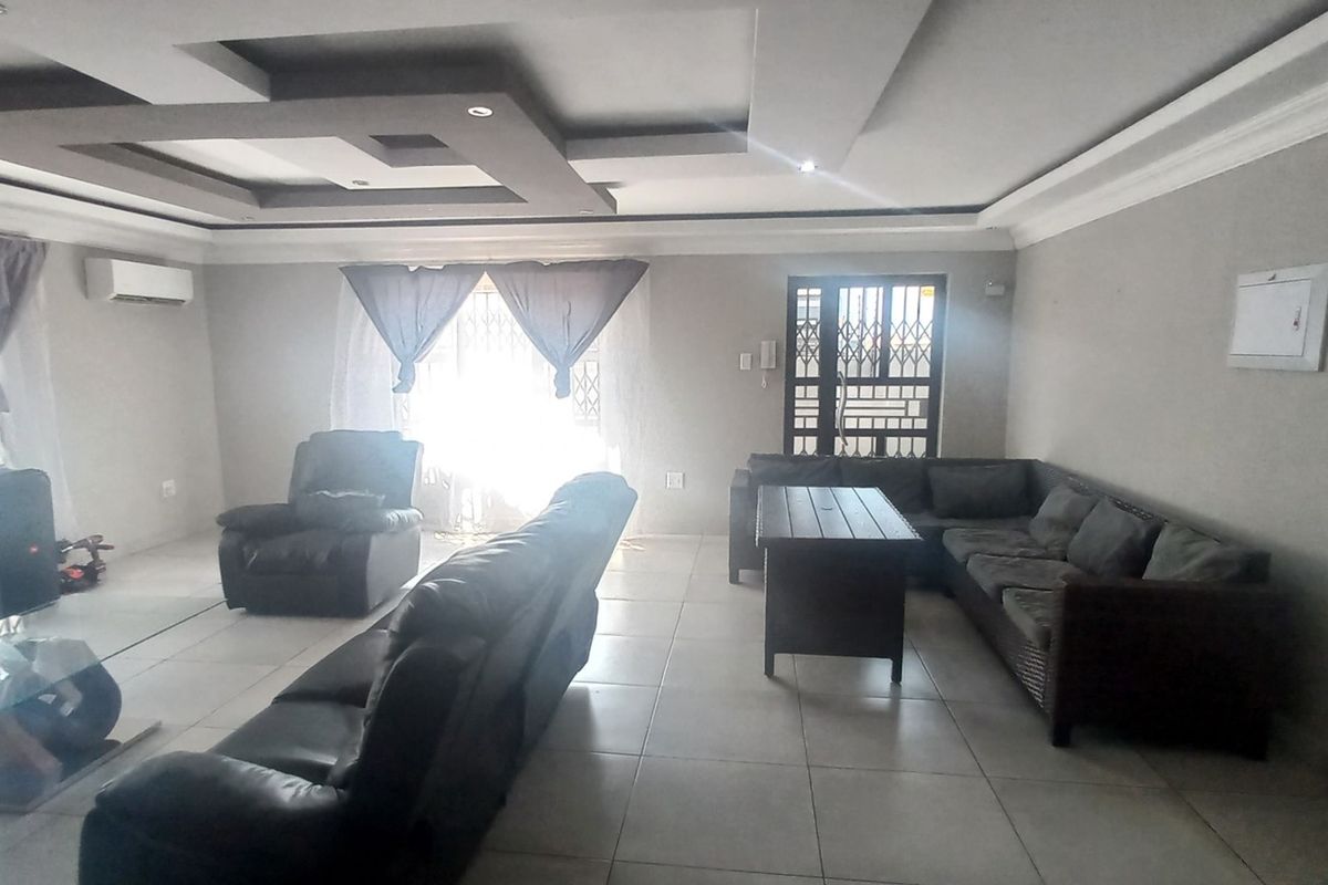 Spacious living room featuring tiled flooring, a modern recessed ceiling with cove lighting, and a wall-mounted split-system air conditioner.