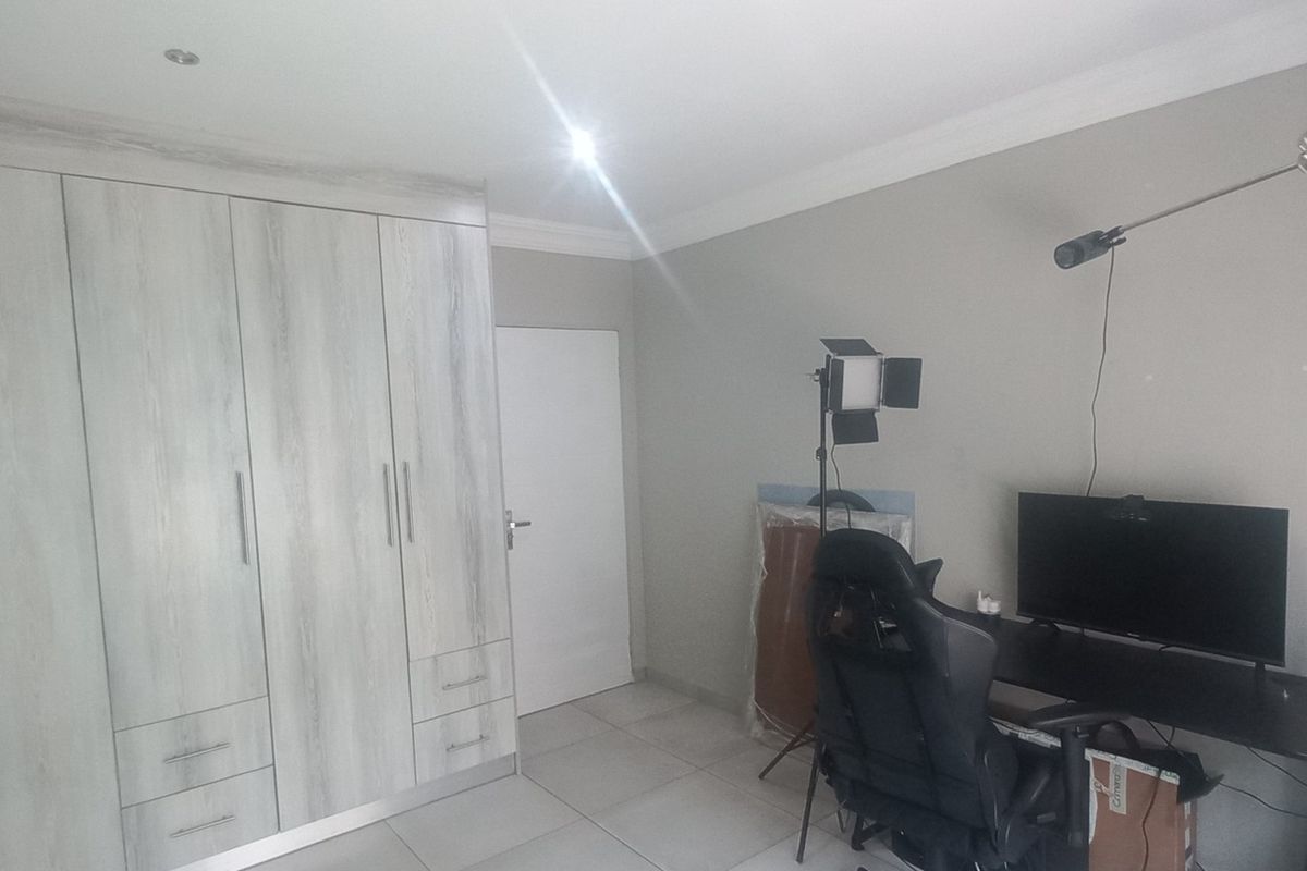 A bedroom featuring modern light wood-grain built-in cupboards, neutral wall finishes, and tiled flooring.