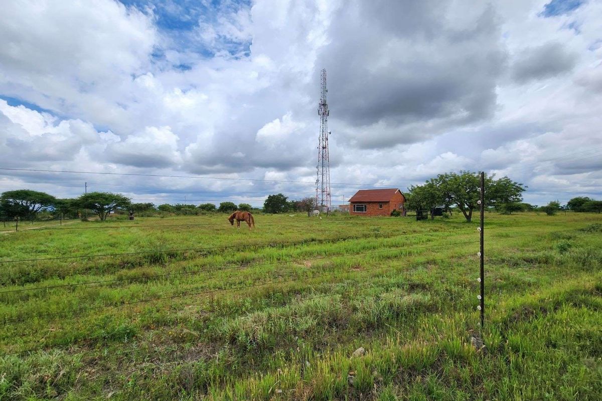 A wide view of the small holding property featuring open grazing land, wire fencing, and a prominent telecommunications mast in the background.