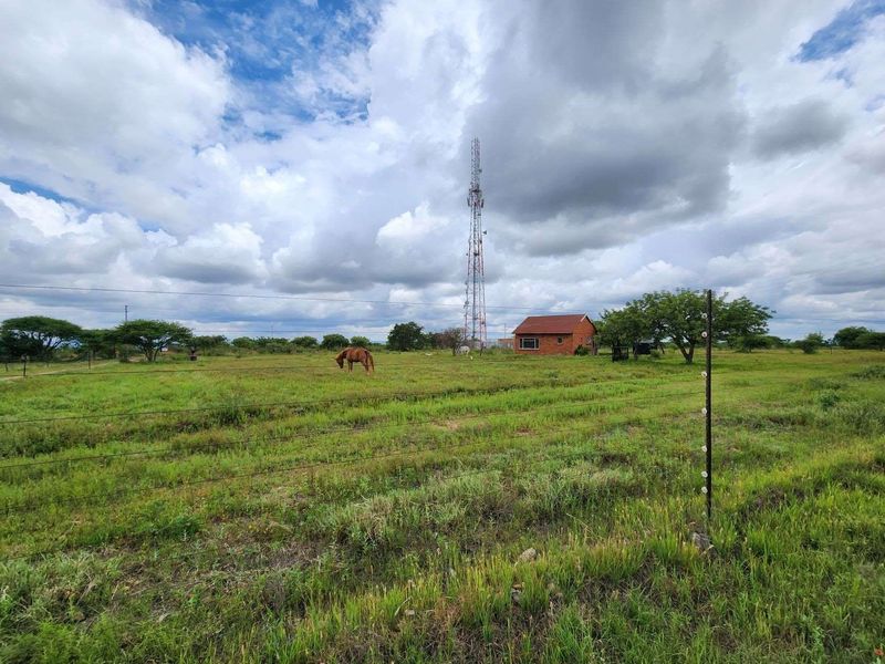A wide view of the small holding property featuring open grazing land, wire fencing, and a prominent telecommunications mast in the background.