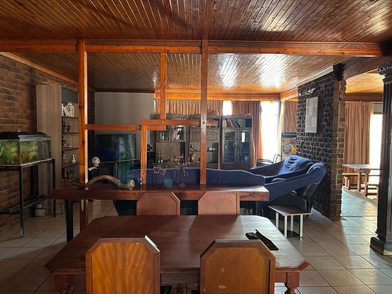 Open plan living and dining area featuring exposed brick walls, tiled flooring, and a prominent timber ceiling with a wooden room divider.