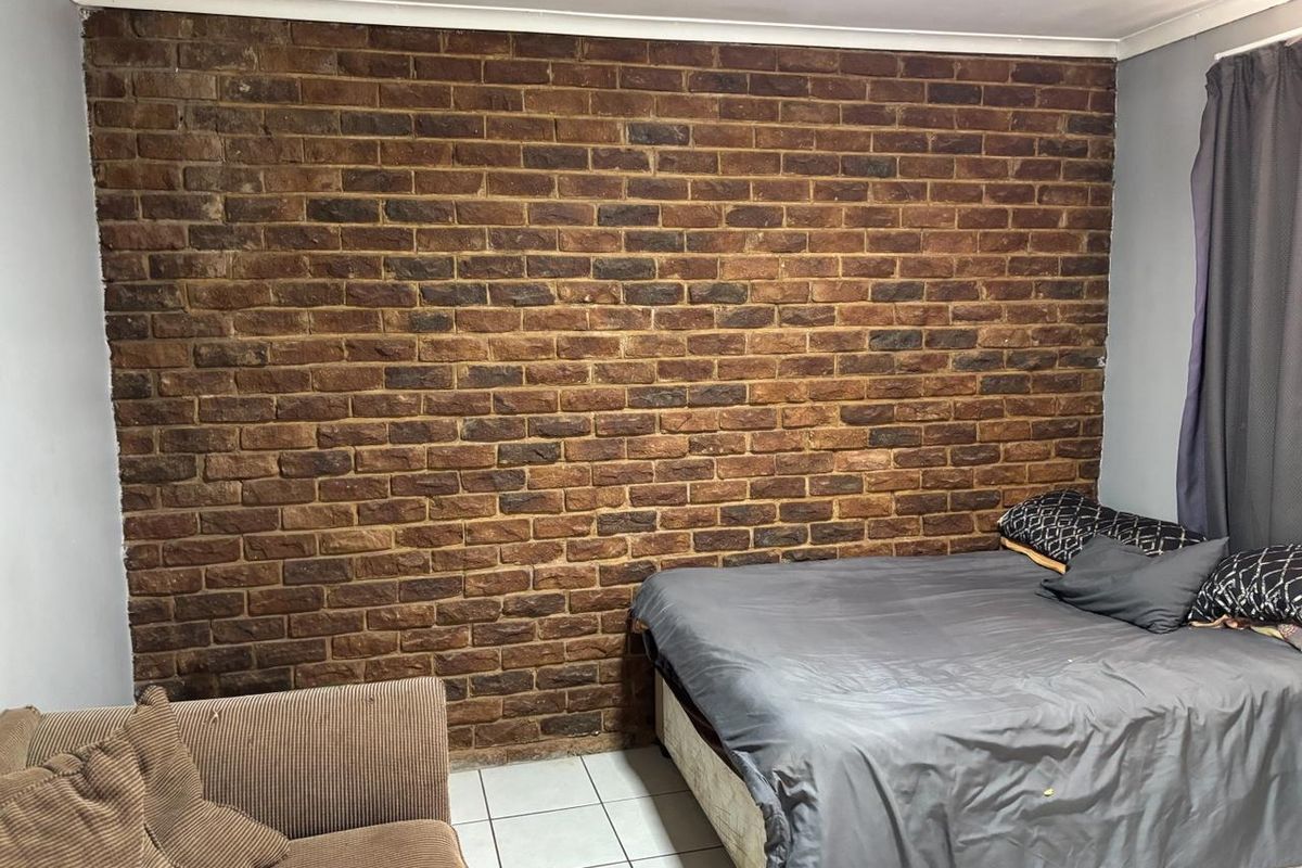 A bedroom featuring a prominent exposed brick feature wall and tiled flooring, providing a rustic aesthetic foundation for the space.