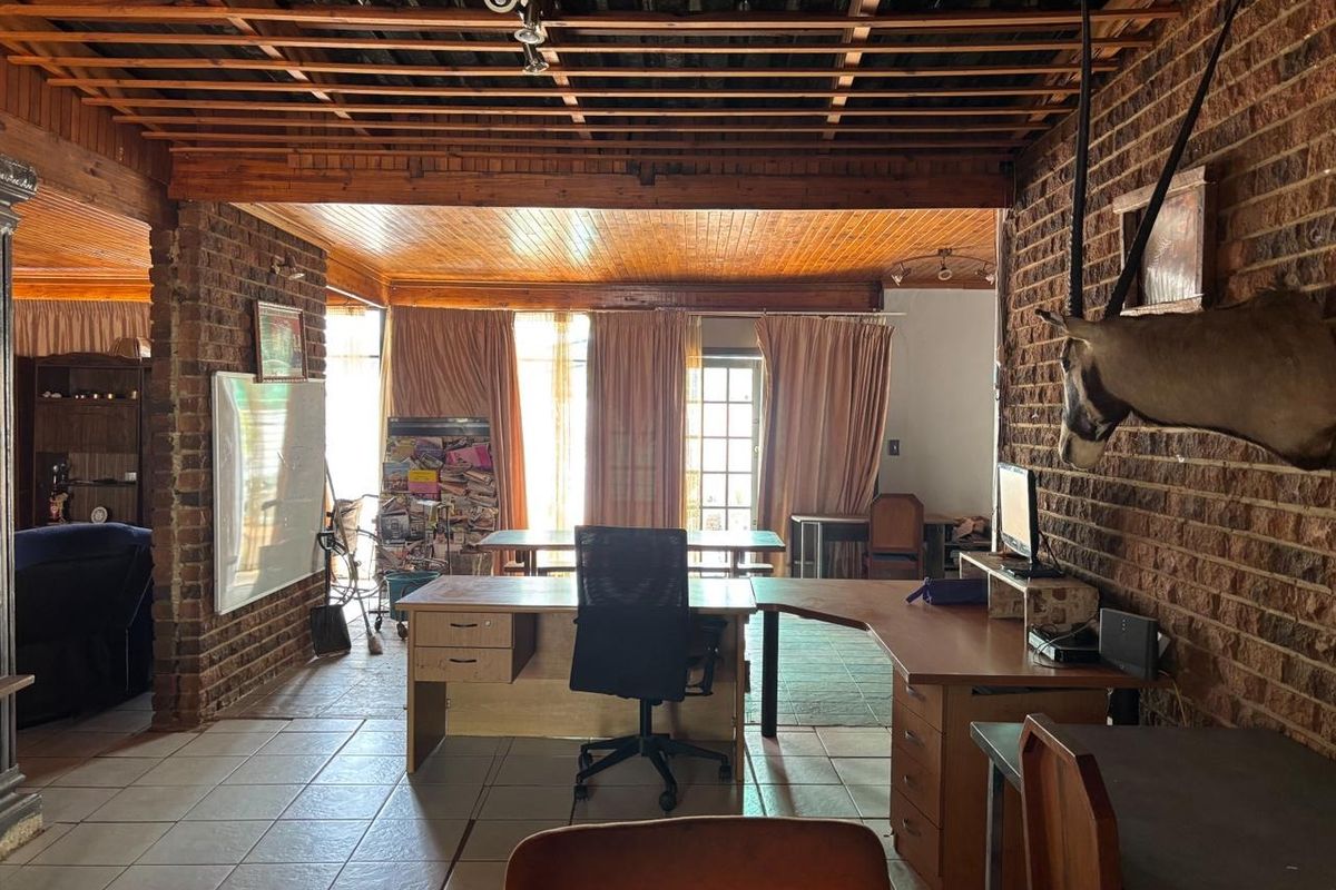 Spacious living area featuring exposed brick walls, timber slat ceiling, and tiled flooring with access to the exterior through french doors.