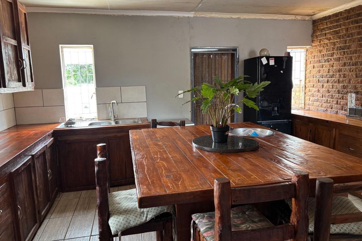 Kitchen featuring wooden cabinetry, a central wooden island, double basin sink, and exposed brick wall detail with tiled flooring.
