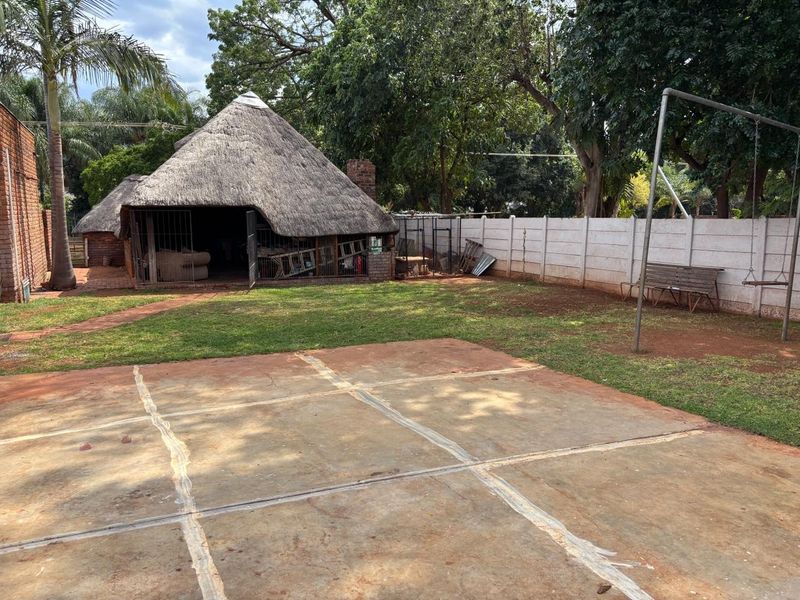 Spacious rear garden featuring a traditional thatched lapa, concrete paved patio area, and secure precast boundary walling.
