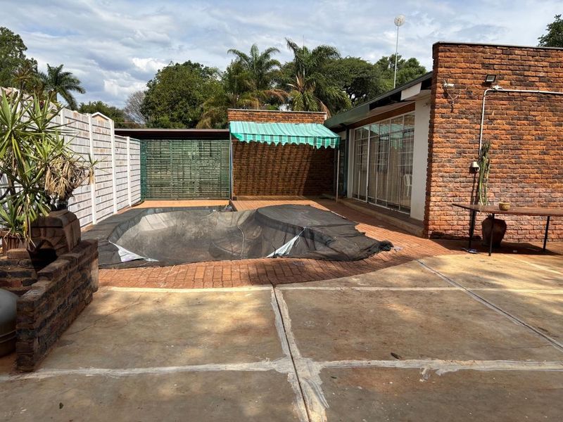 Outdoor pool area featuring a covered swimming pool, brick paving, and an exposed brick facade with a retractable awning.