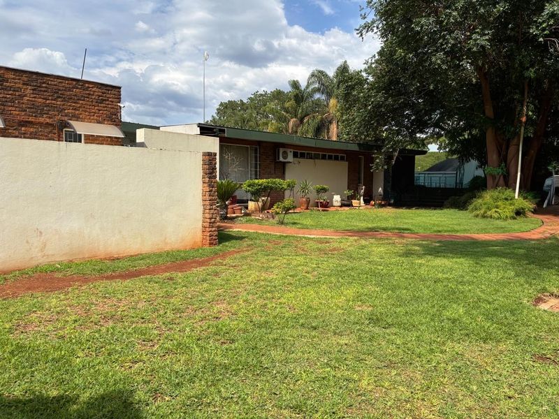 A view of the rear garden featuring a lawn, paved walkway, and brick boundary wall with an exterior air conditioning unit mounted on the house.