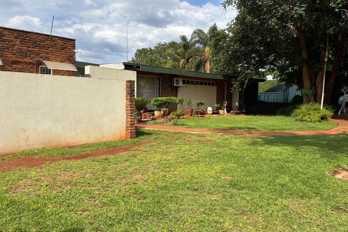 A view of the rear garden featuring a lawn, paved walkway, and brick boundary wall with an exterior air conditioning unit mounted on the house.