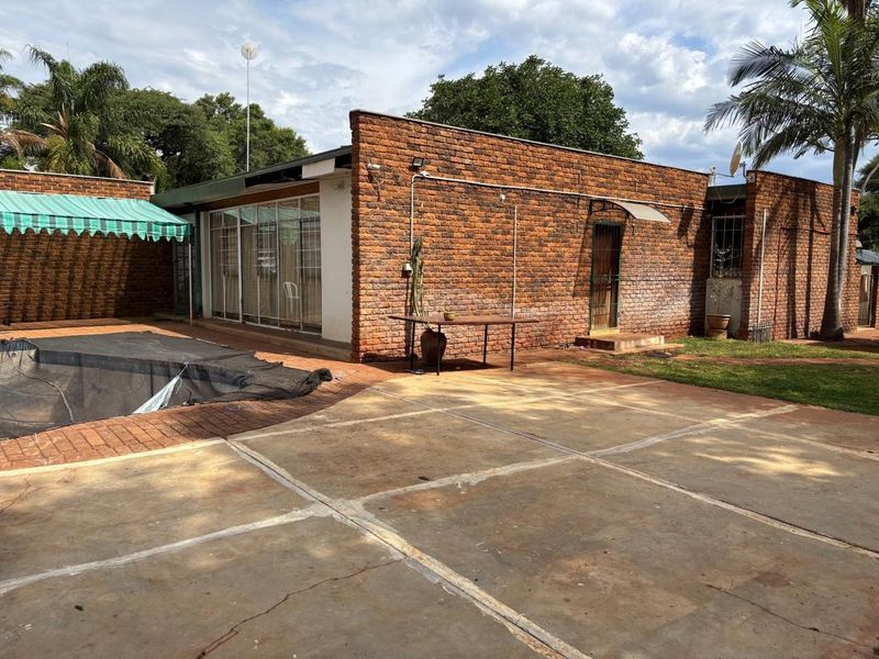 Rear exterior view featuring an exposed brick facade, concrete patio area, swimming pool, and sliding glass door access to the main living space.