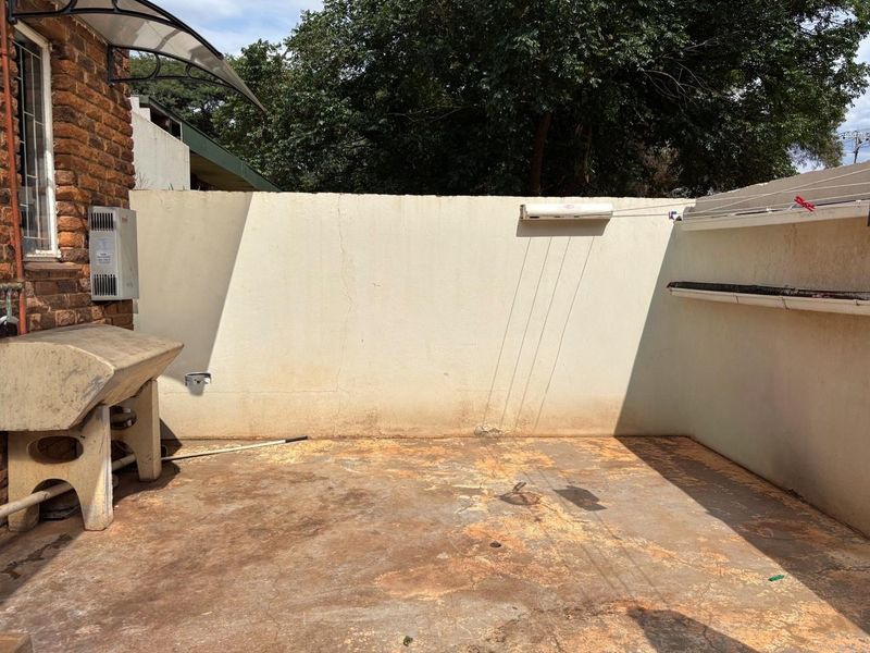 An outdoor laundry area featuring a concrete wash trough, wall-mounted drying rack, and concrete flooring, requiring maintenance and surface repairs.