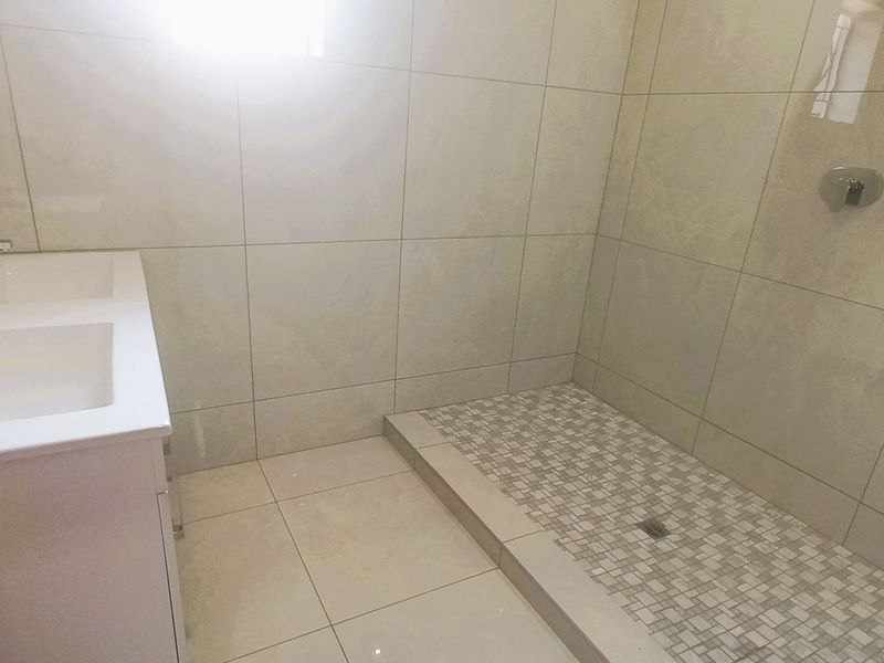 Modern bathroom featuring a double vanity with basin mixers and a spacious walk-in shower with tiled finishes.