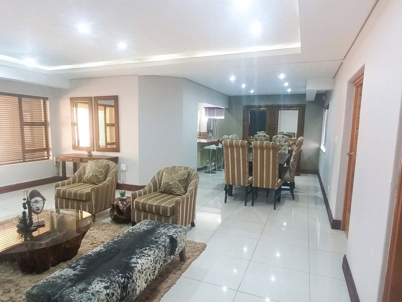 Spacious open-plan living and dining area featuring polished tiled floors, recessed ceiling lighting, and large windows with wooden blinds.