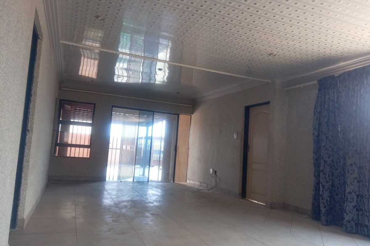 An empty living room featuring tiled flooring, a glossy panel ceiling, and a sliding glass door providing access to the exterior.